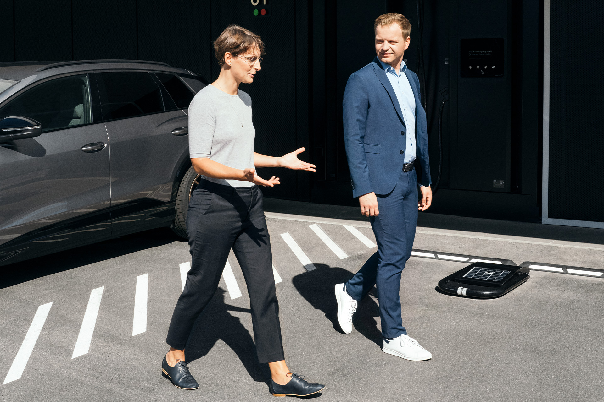 Los expertos en sostenibilidad, la Dra. Johanna Klewitz y Malte Vömel, cruzan el aparcamiento frente al centro de carga de Audi en Núremberg.
