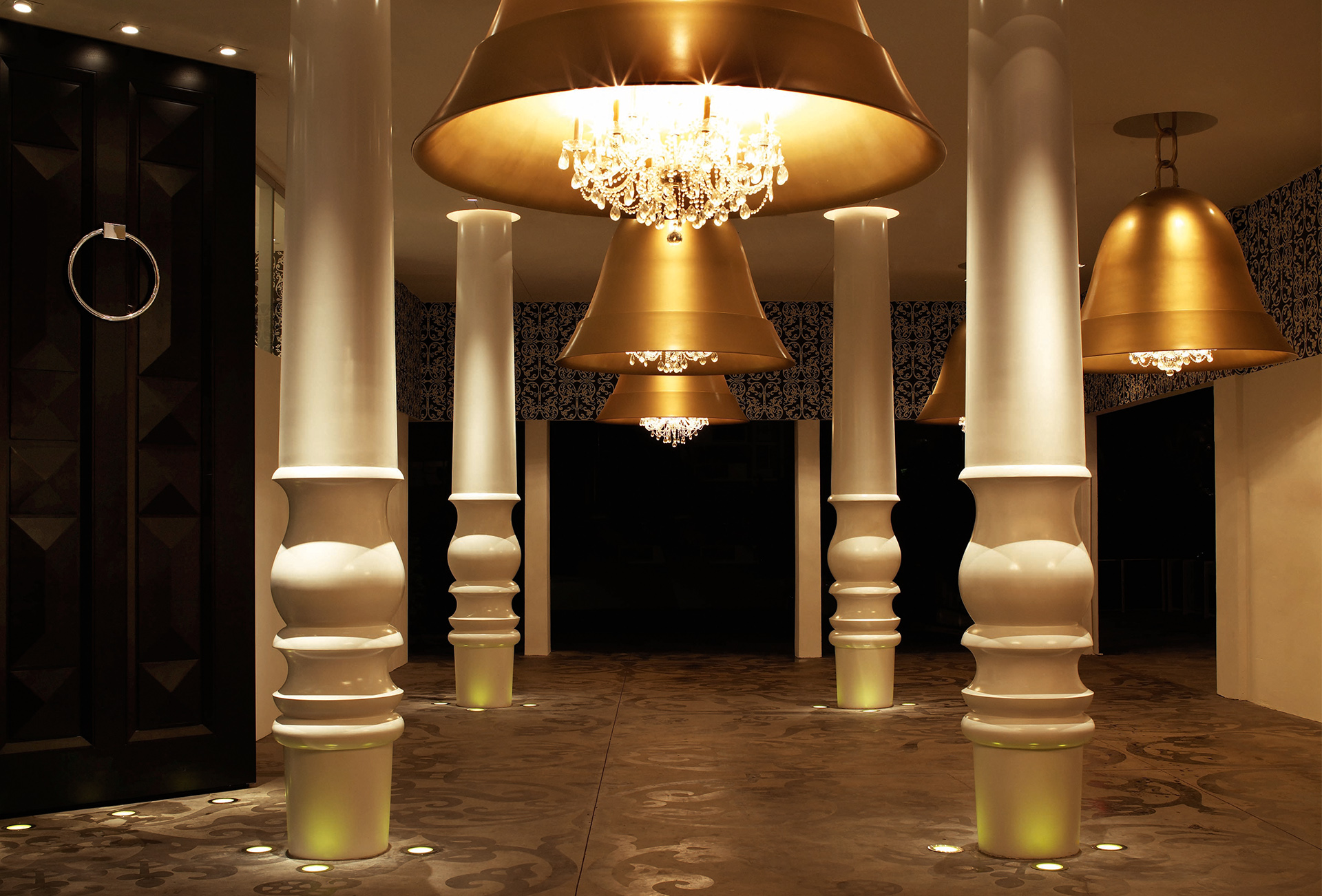 Enormes lámparas de campana doradas cuelgan en un pasillo entre columnas blancas.