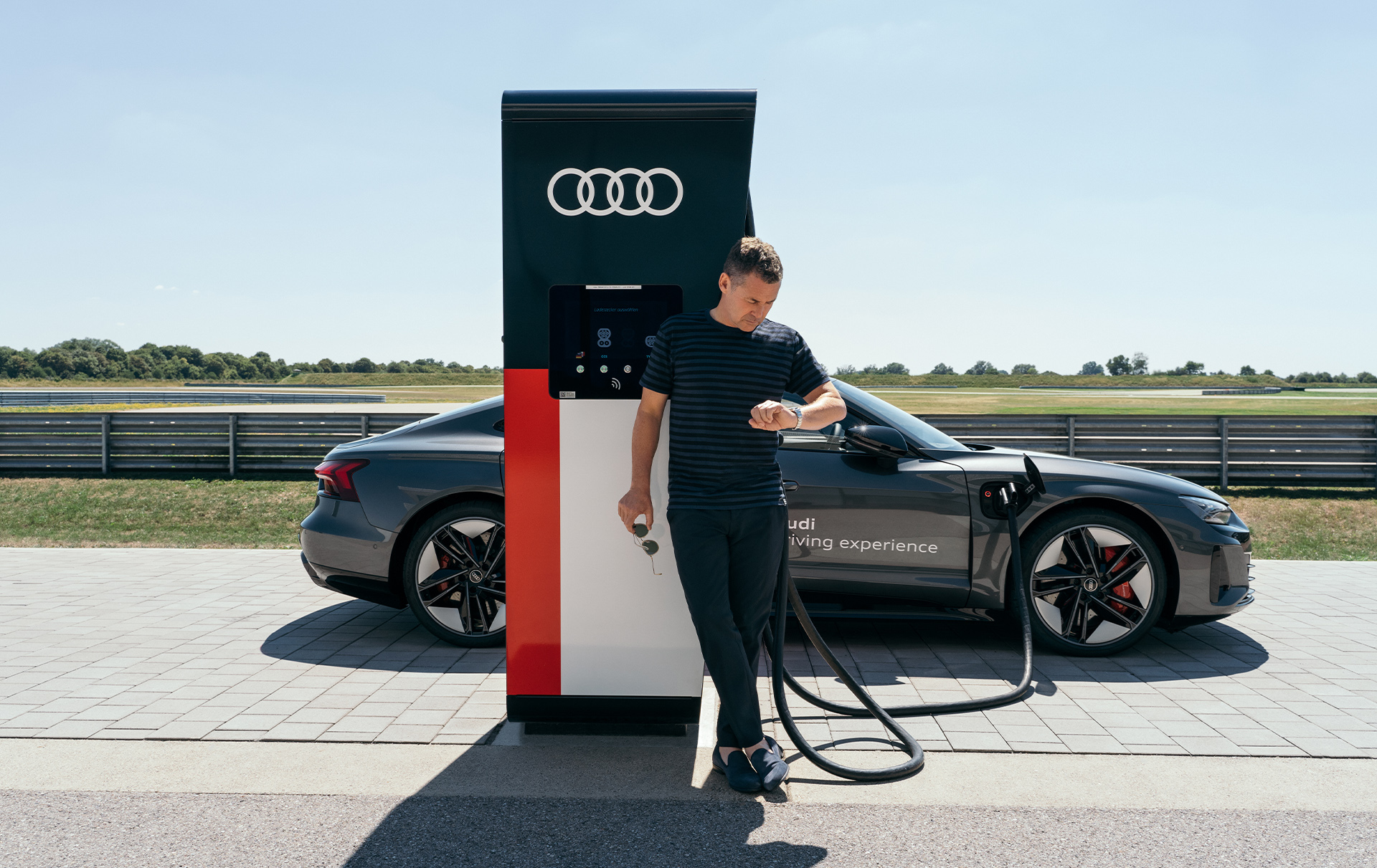 Tom Kristensen se apoya en un punto de carga eléctrica mientras el Audi RS e-tron GT se carga.