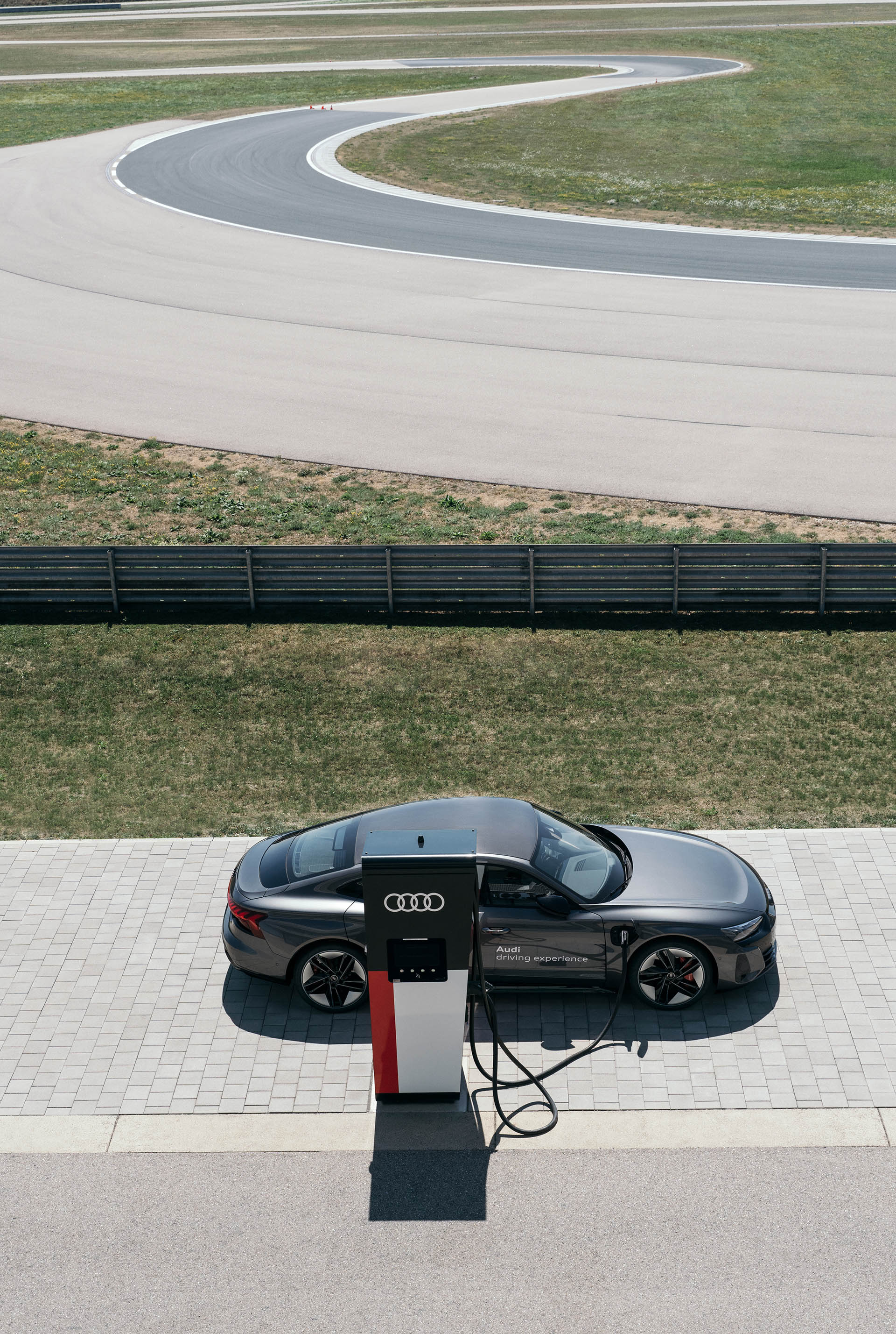 En primer plano, el Audi RS e-tron GT carga y, al fondo, se ve el circuito de carreras.